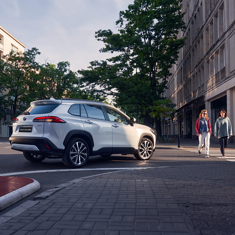 şehir içinde yayaların geçmesini bekleyen yeni Toyota Corolla Cross Hybrid yan görünüşü