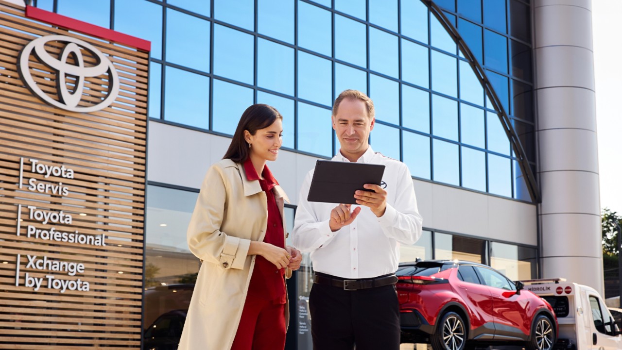 dış mekanda bir müşteriyle tablet üzerinden araç servisi ve bakım işlemleri hakkında bilgi paylaşan Toyota servis danışmanı